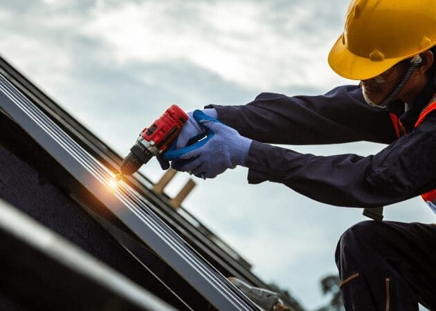 Worker installing roof using power drill.